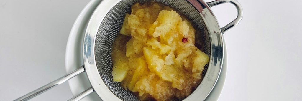 Apple mash in a sieve over a bowl